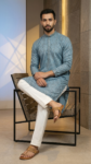 Men's dusty blue Lucknowi Chikankari kurta with intricate embroidery and mirror work, paired with white trousers and tan sandals (1)