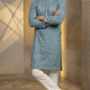 Men's dusty blue Lucknowi Chikankari kurta with intricate embroidery and mirror work, paired with white trousers and tan sandals (1)