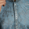 Men's dusty blue Lucknowi Chikankari kurta with intricate embroidery and mirror work, paired with white trousers and tan sandals (1)